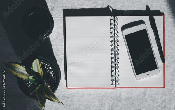 Fototapeta Workspace with mobile phone,notebook,pen,coffee cup and house plant on white background,top view