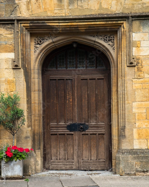 Fototapeta Large old arched door way with cast iron furniture.  Deep set doorway set into yellow stone building with plants and flowers outside