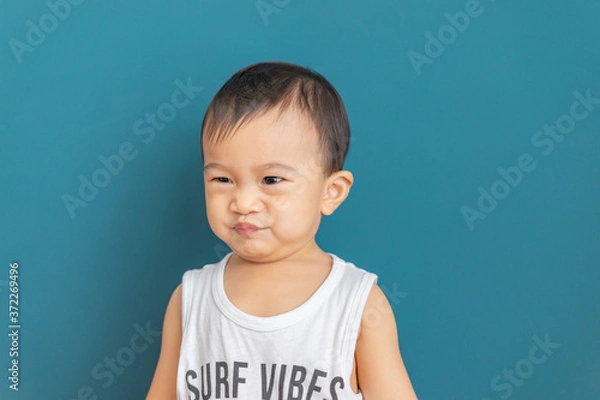 Fototapeta Asian little boy makes a cheeky face on blue background,Happy childhood.