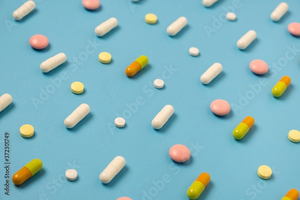 Fototapeta Close up of many different pills arranged in pattern on blue background.