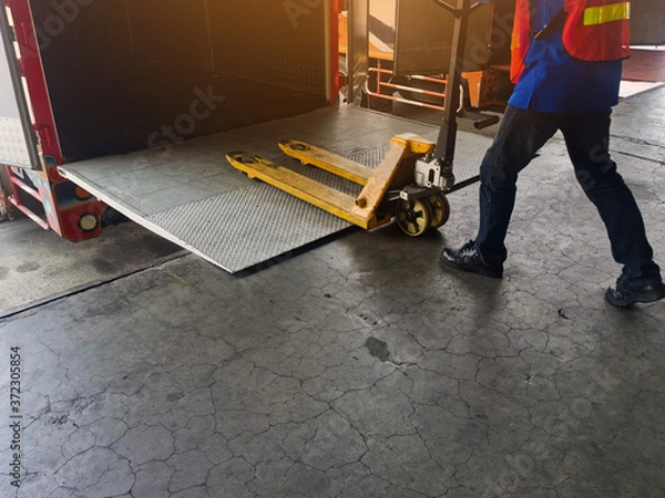 Fototapeta Worker driving forklift loading shipment carton boxes and goods on wooden pallet at loading dock from container truck to warehouse cargo storage in freight logistics and transportation industrial
