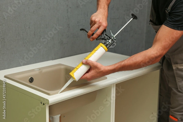 Fototapeta refurbishment in the apartment. kitchen sink sealing close up. worker's hands working with construction sealant gun in the kitchen