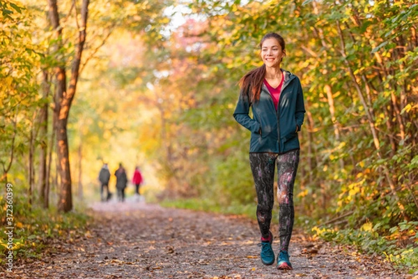 Fototapeta Woman walking in autumn forest nature path walk on trail woods background. Happy girl relaxing on active outdoor activity.