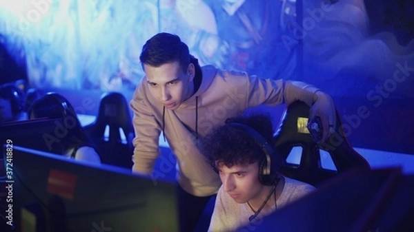 Obraz Pro Gamers trainer giving advice to his friend while he is playing round of video game in modern cybersport club
