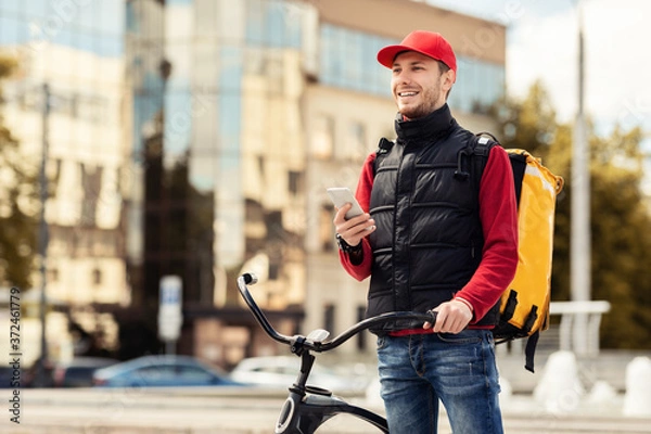 Fototapeta Positive Courier With Smartphone Using Delilvery App Working In City