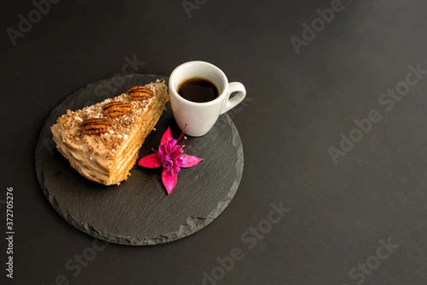 Obraz A typical Portuguese cake made of cookies called Bolo de Bolasa with cream, pecans, black and white chocolate on a black slate with espresso cup and a flower on a black background. Free space for text