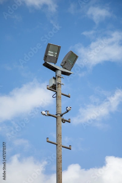 Fototapeta Floodlights above a football pitch with blue sky and clouds in the background