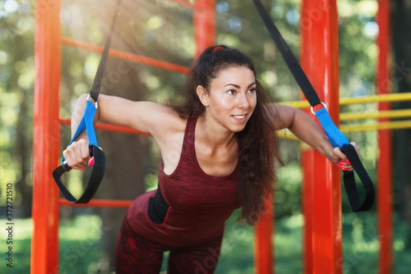 Fototapeta Young brown-haired woman goes in for sports with fitness belts in the park. Concept on the topic of a healthy lifestyle