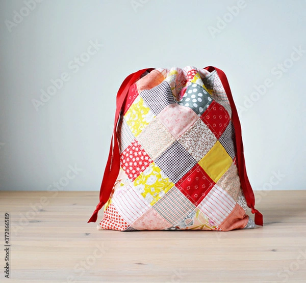 Fototapeta Colorful patchwork drawstring bag on wooden table and white wall