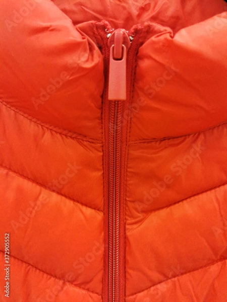 Fototapeta Close-up on orange puffer jacket texture with a zipper and a runner close-up