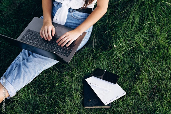 Fototapeta student girl with laptop outdoors sitting on the grass, surfing the internet or preparing for exams. Technology, education and remote work concept. Soft selective focus.