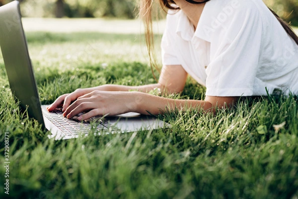 Fototapeta student girl with laptop outdoors. woman lying on the grass with a computer, surfing the Internet or preparing for exams. Technology, education and remote work concept. Soft selective focus.