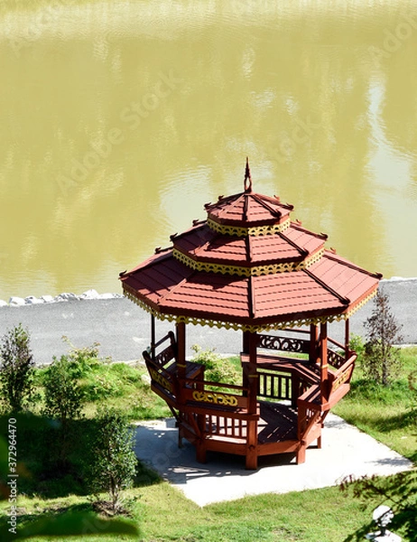 Fototapeta Thai wooden pavilion stands outstandingly beside the pond and jogging track.