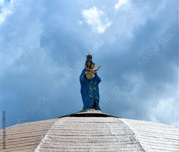 Fototapeta A statue of the Virgin Mother Mary carrying the baby Jesus stands on top of a white dome of a church