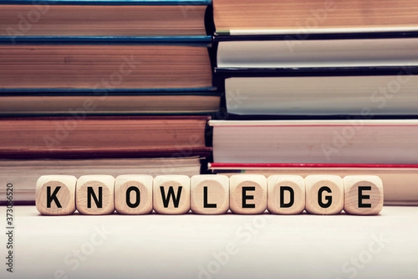 Fototapeta The word knowledge on wooden cubes with stacked books background. Education, wisdom and learning concept.