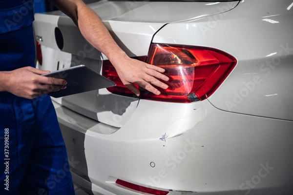 Fototapeta Mechanic in uniform inspects the bumper of the car