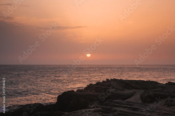 Fototapeta Beautiful sunset on the sea with the sun going down on the horizon and rocks in the foreground.