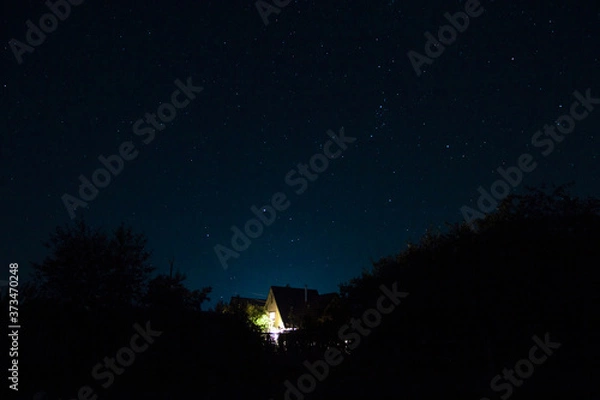 Obraz Starry night sky, and a wooden cottage with lights in the Windows