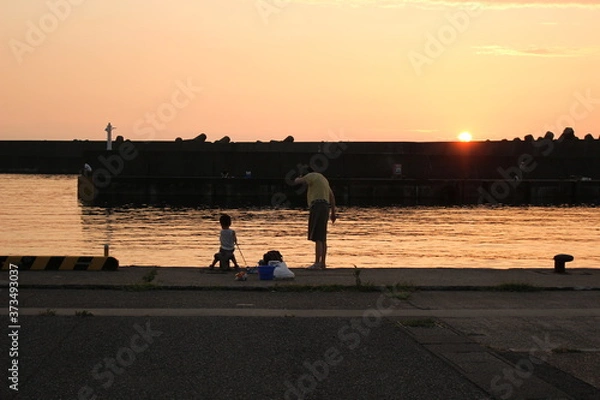 Obraz 夕暮れの港で堤防釣りをする子供と母親