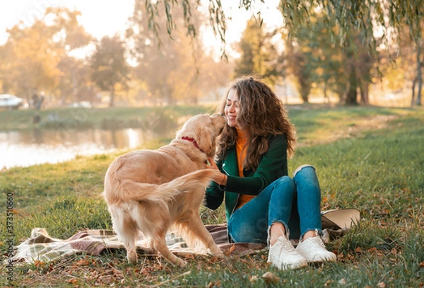 Fototapeta Smiling woman hugging her pet golden retriever dog near face. Golden retriever dog playing with a curly woman walking outdoors sunny day. love and care for the pet.