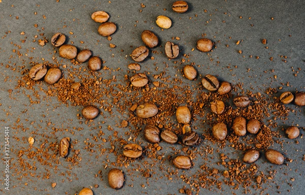 Fototapeta Coffee beans and ground coffee beans scattered on a black background in a warm tone