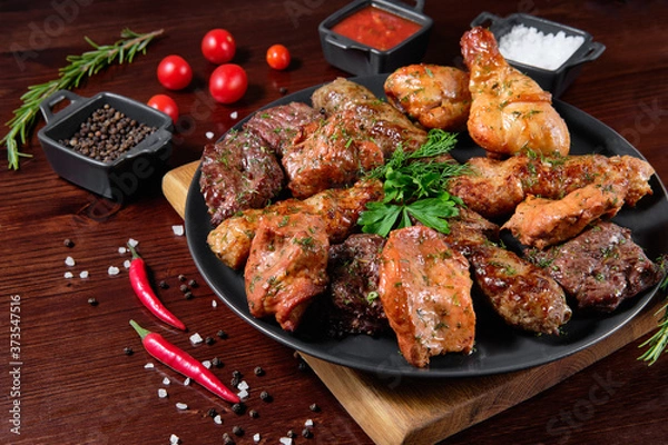 Fototapeta Assorted delicious grilled meat with vegetable. Mixed grilled bbq meat with vegetables. Set of shish kebabs or barbecue shashlik collection. Baked potatoes and fresh tomatoes. Various sauces for meat.