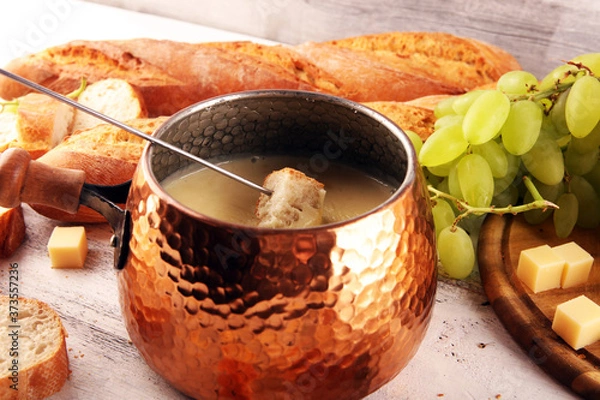 Fototapeta Gourmet Swiss fondue dinner on a winter evening with assorted cheeses on a board alongside a heated pot of cheese fondue with two forks dipping