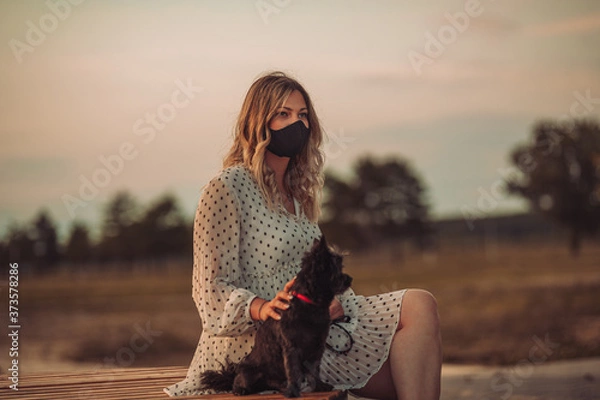 Fototapeta The girl enjoys walking with the dog and wears a mask on her face