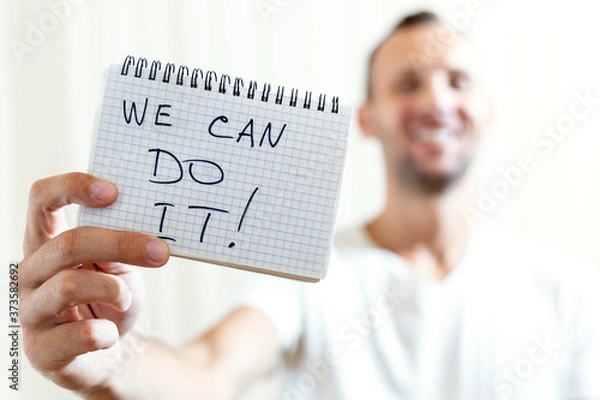Obraz blurred man holds in his outstretched hand a sheet of paper with the inscription WE CAN DO IT