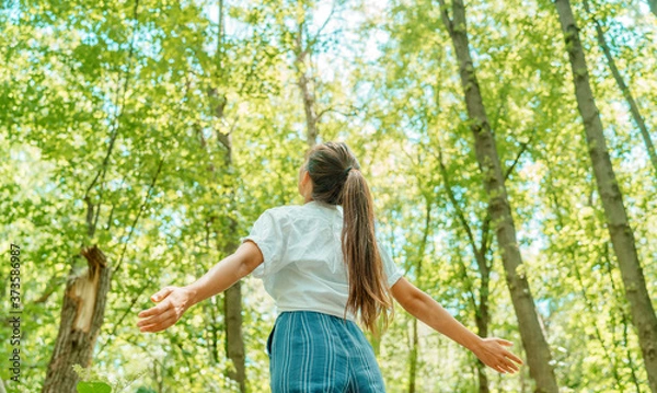 Fototapeta Wolna kobieta oddychająca czystym powietrzem w lesie natura. Szczęśliwa dziewczyna z tyłu z otwartymi ramionami w szczęściu. Świeże lasy na świeżym powietrzu, koncepcja zdrowego stylu życia.