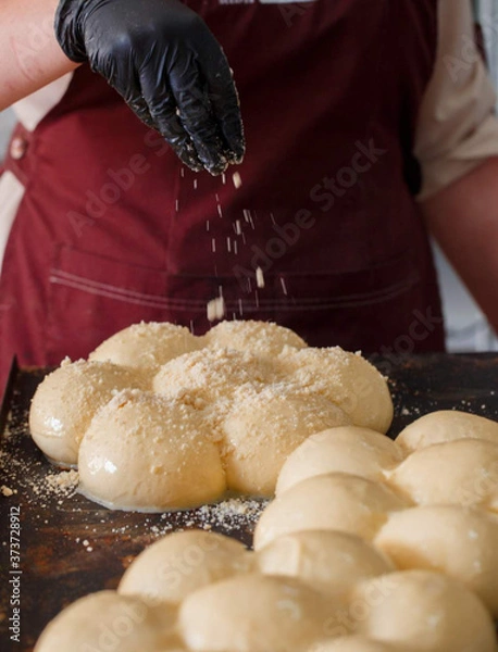 Fototapeta a Baker in a red apron sprinkles dough pieces that are lying on a baking sheet