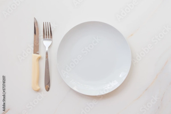 Fototapeta  Empty white plate with cutlery on a marble table, saucer, fork and knife. The concept of diet, fasting