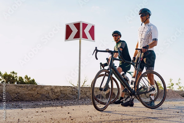 Fototapeta Two male cyclists stand on the road and have a rest