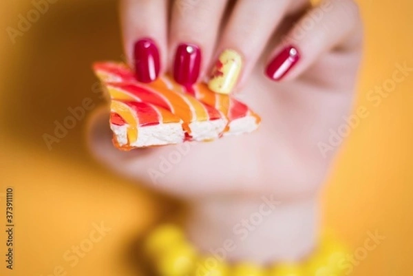 Fototapeta a woman's hand with a bright manicure holds a piece of multicolored dessert
