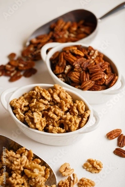 Fototapeta there are plates of walnuts and pecans on the white table