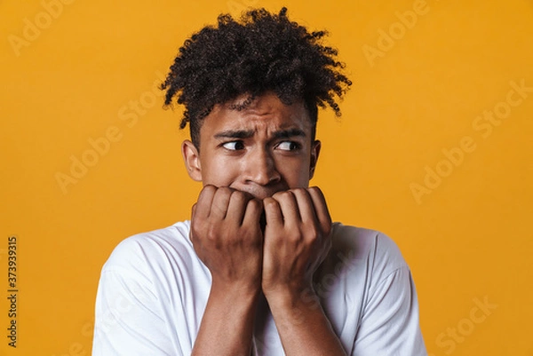 Fototapeta Image of scared african american guy biting his fingernails