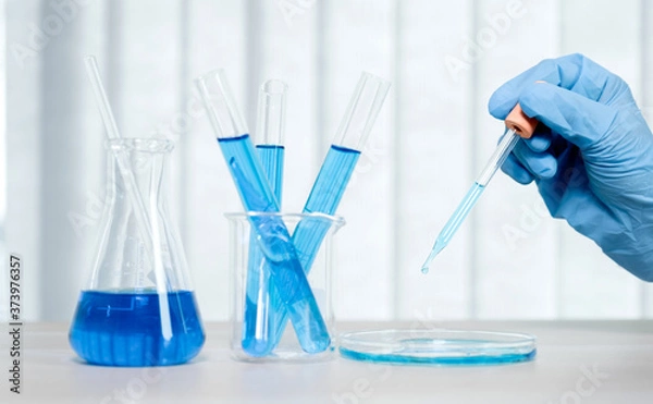 Fototapeta Scientists hold the pipette and drop the blue chemical liquid for research and analysis in a laboratory