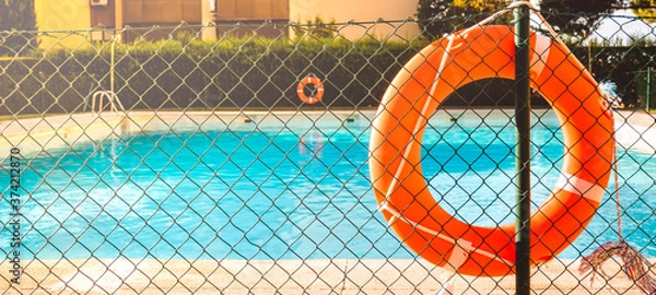 Fototapeta View of a salt water pool from the fence with a orange life float on a sunny summer day.