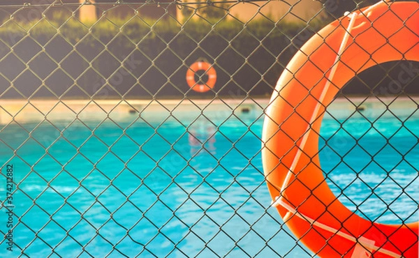 Fototapeta View of a salt water pool from the fence with a orange life float on a sunny summer day.