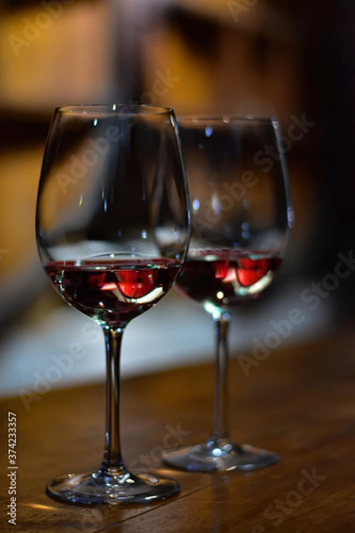 Fototapeta Pair of wine glasses with red wine and wine barrels reflection. Wine tasting in a wine cellar. Vineyard in Mendoza region, Argentina