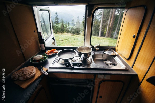 Obraz Interior of travel camping van or camper RV with stove and sink. Vanlife lifestyle vibes, cooking on campsite during road trip with amazing view of mountains. Life on the road in converted van