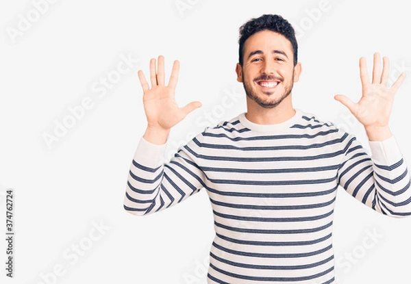 Obraz Young hispanic man wearing casual clothes showing and pointing up with fingers number ten while smiling confident and happy.