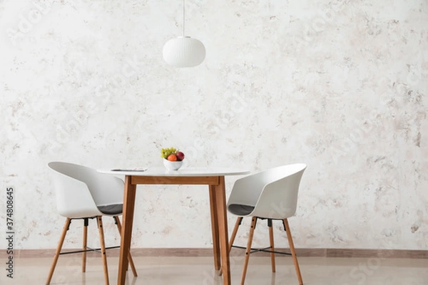 Fototapeta Dining table with fruits in bowl near light wall