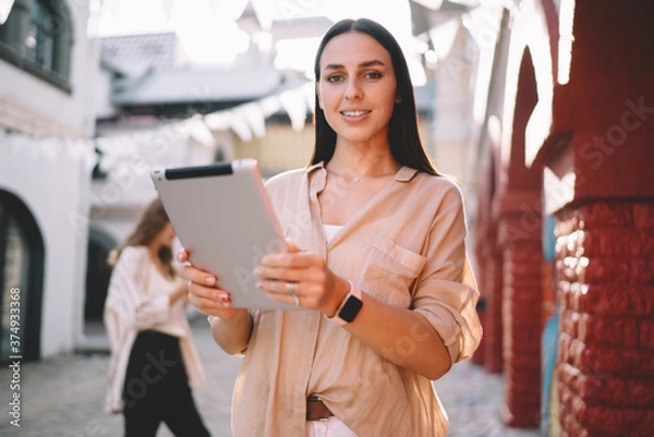 Fototapeta Half length portrait of pretty female with modern digital tablet in hands posing at urbanity, successful Caucasian blogger 20 years old with touch pad smiling at camera during sunny day in city