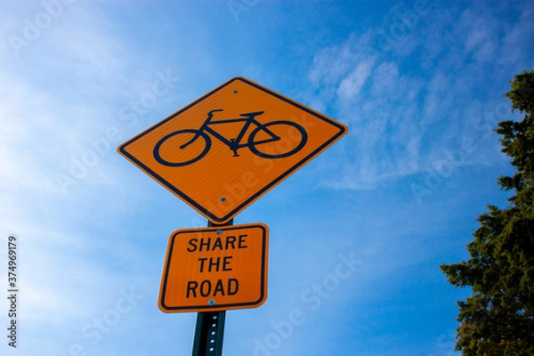 Obraz  Bug eye view of a yellow rhombus road sign with a bicycle symbol, and a plate attached underneath which says 'share the road'