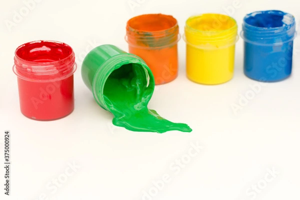 Fototapeta multicolored cans of gouache stand in a row on a white background, one may have fallen and green paint spilled out of it. Horizontal photo, close-up.