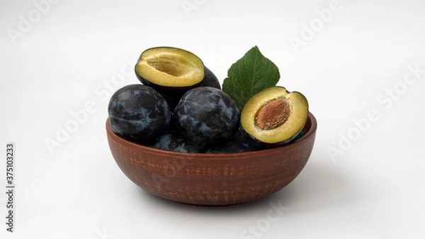 Fototapeta Plums lie in a ceramic bowl  on a white background
