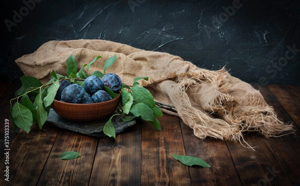 Fototapeta Plums lie in a ceramic bowl on a wooden table against a background of black slate