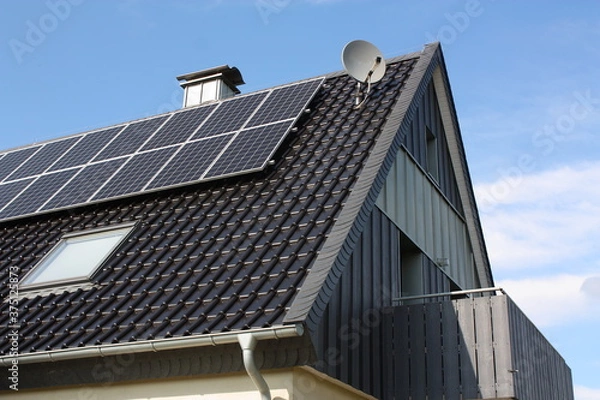 Fototapeta Photovoltaikanlage auf einem Haus mit Balkon, Kaminabdeckung und Satellitenschüssel, bei blauem Himmel und Sonnenschein, in Lippetal Büninghausen an der Buschstraße