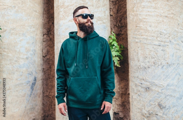 Obraz City portrait of handsome hipster guy with beard wearing green (watercolor) blank hoodie or sweatshirt with space for your logo or design. Mockup for print